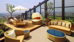 A rooftop terrace with wicker furniture, a glass table, and a view of the city. - Sheraton Grand Adana (Adana)