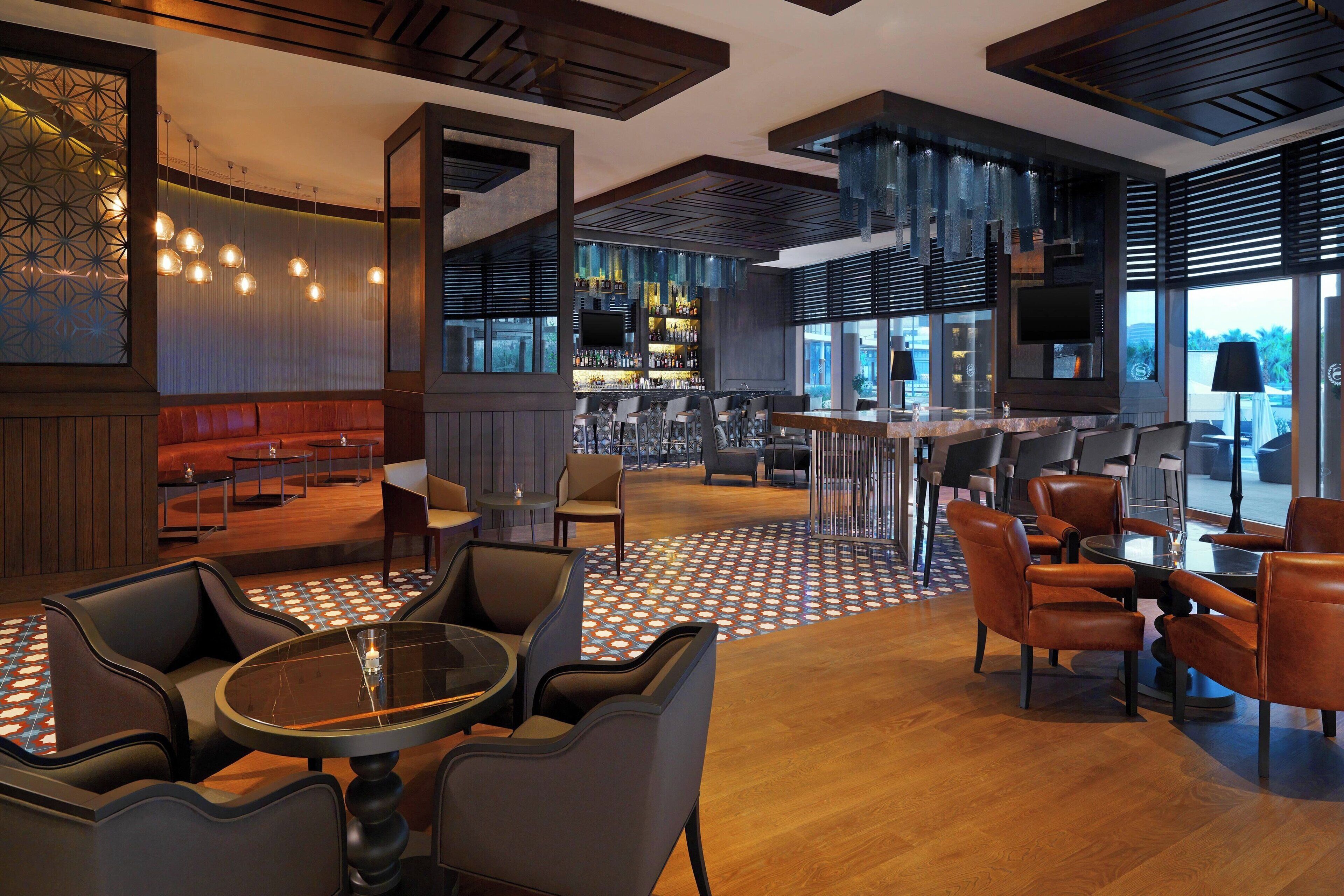 A modern bar area with seating, a patterned floor, and a large TV screen.
