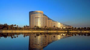 A modern hotel with a curved facade, reflecting in a calm body of water. - Sheraton Grand Adana (Adana)