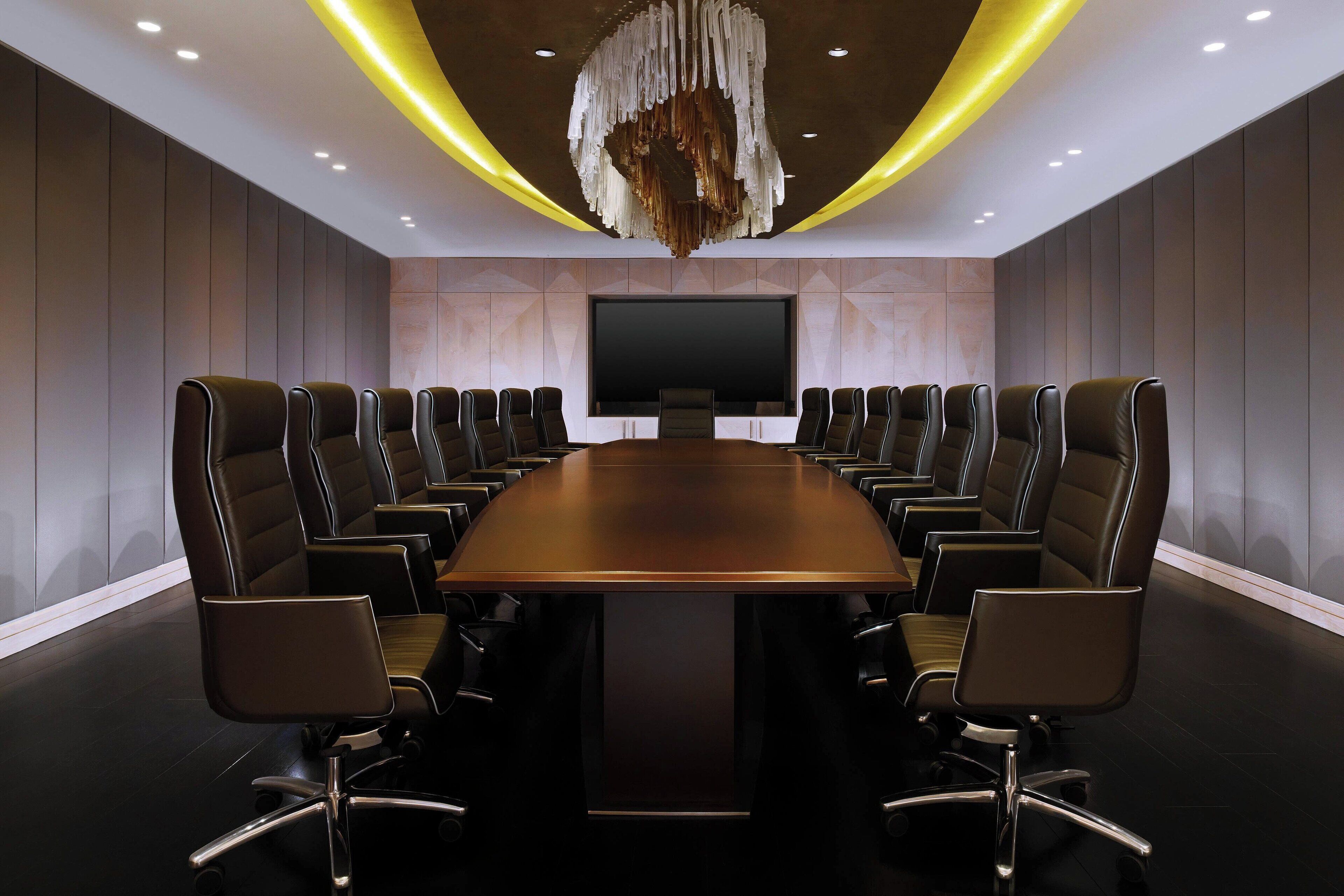 Een congrescentrum met een lange tafel en 12 stoelen, een groot scherm en een bijzondere kroonluchter.