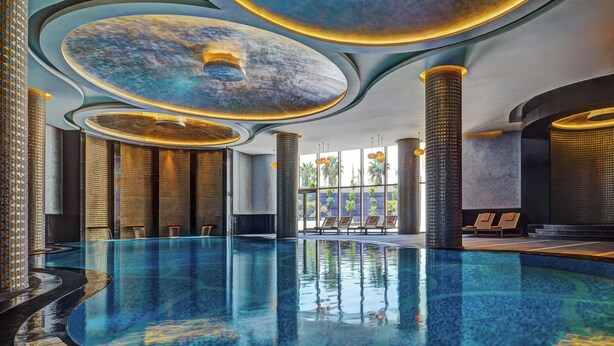 A large indoor swimming pool with a modern design, surrounded by lounge areas and large windows. - Sheraton Grand Adana (Adana)