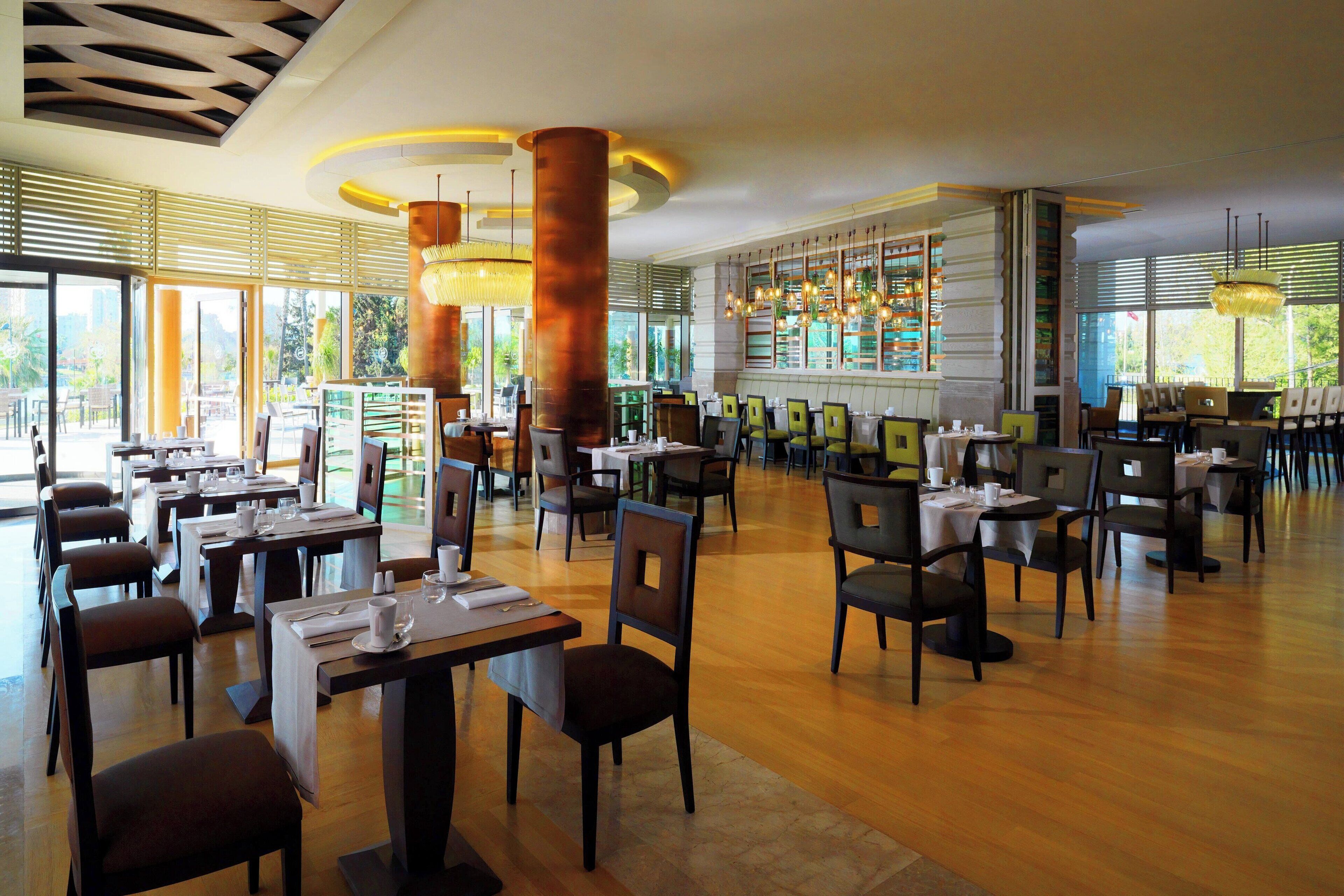 A spacious restaurant with multiple dining tables and chairs, large windows, and modern lighting fixtures.
