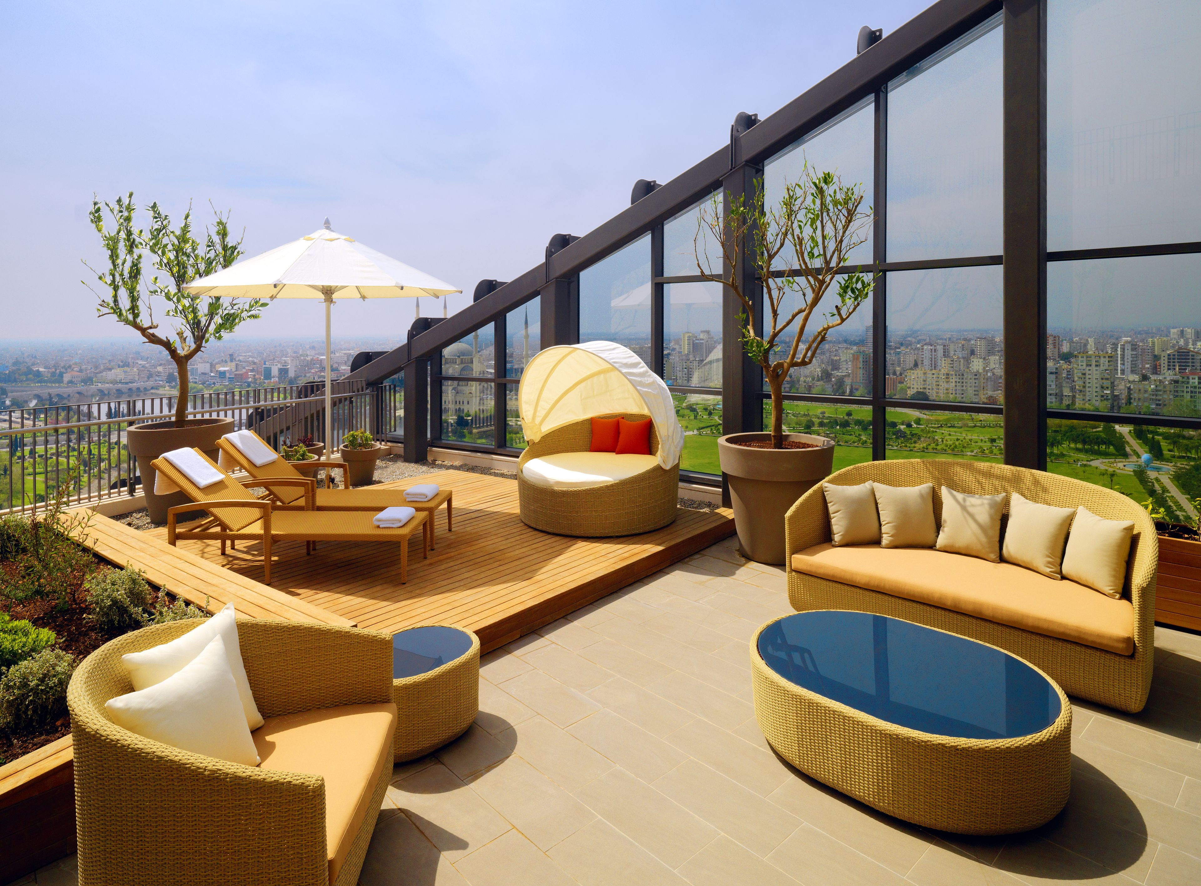 A rooftop terrace with wicker furniture, a glass table, and a view of the cityscape.