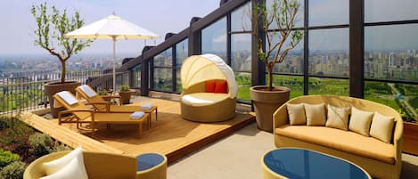 A rooftop terrace with wicker furniture, a glass table, and a view of the cityscape.