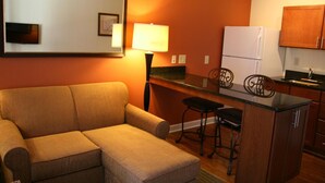 Un espacio habitable compacto con sofá, una pequeña cocina con refrigerador y un taburete de bar.