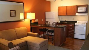 Un espacio habitable compacto con sofá, pequeña cocina con estufa y microondas, y una mesa de comedor con sillas.