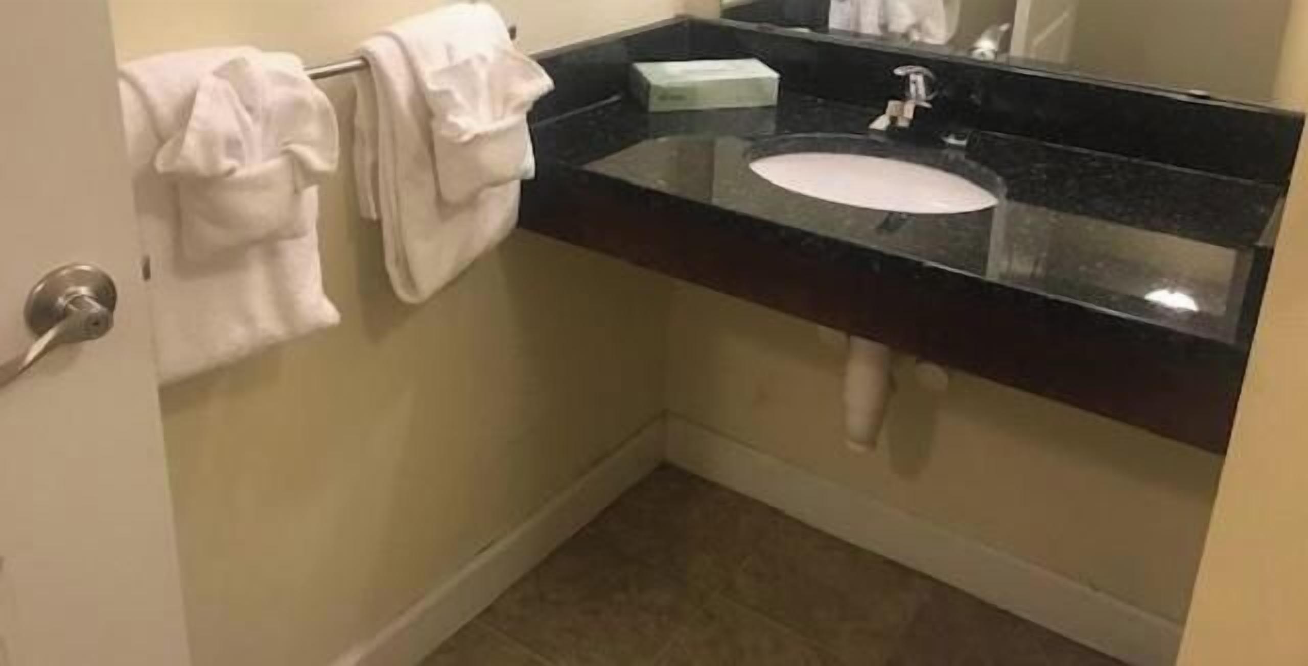 Une salle de bain avec un comptoir noir, un lavabo blanc et un porte-serviettes avec des serviettes.