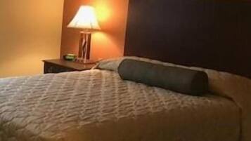 Una cama bien hecha con colcha, una lámpara de noche y un cuadro en la pared.