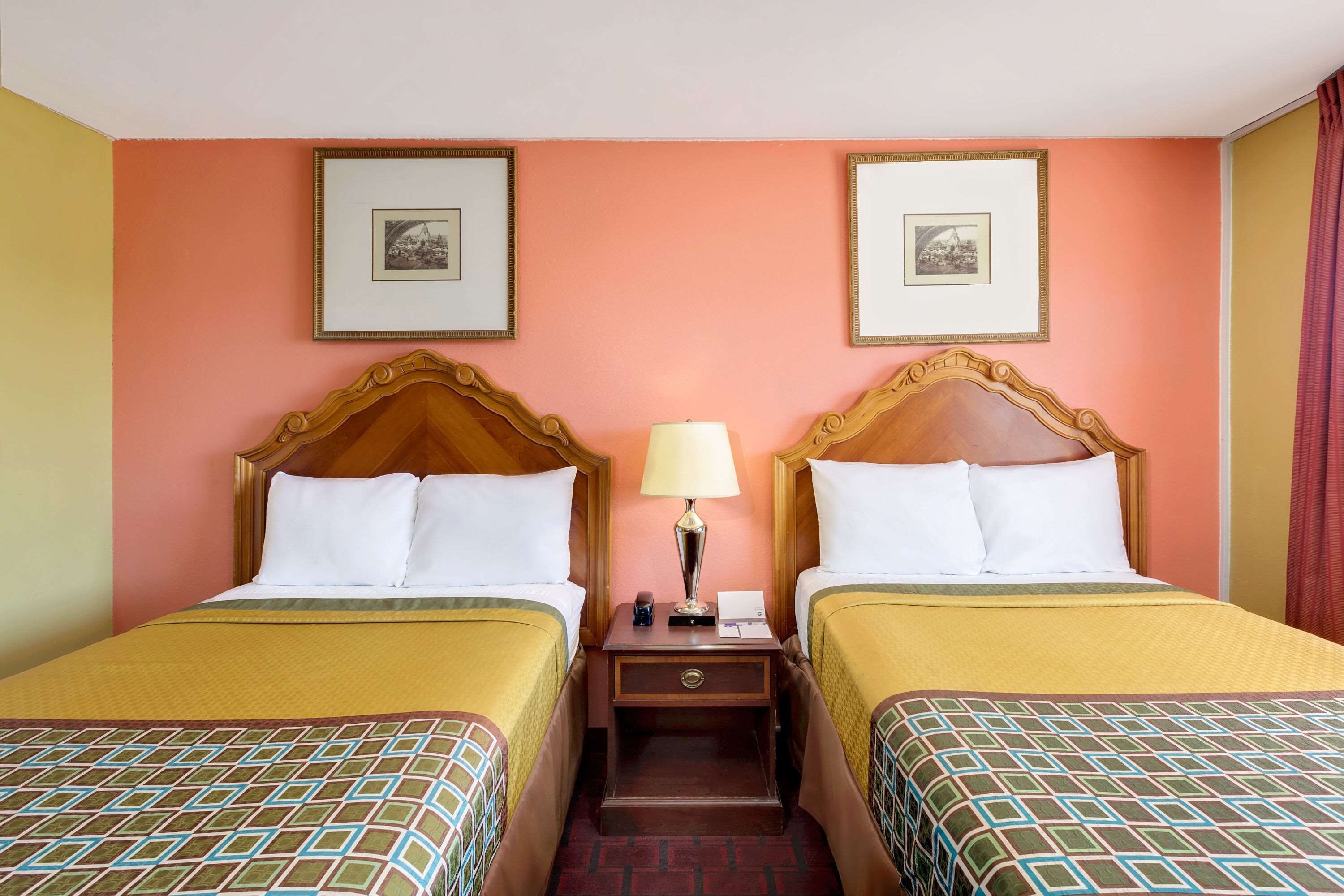 Een hotelkamer met twee bedden, een nachtkastje met een lamp, en ingelijste foto's aan de muur.