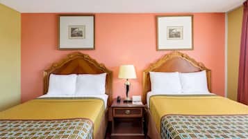 Een hotelkamer met twee bedden, een nachtkastje met een lamp, en ingelijste foto's aan de muur.