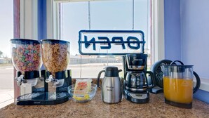 A kitchen counter with a coffee maker, a milk jug, a blender, and two cereal dispensers.