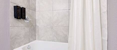 Un baño con bañera, cabezal de ducha y un juego de artículos de aseo.