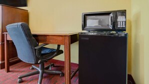 A compact office space with a desk, a black office chair, a microwave, and a television mounted on the wall.