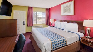 A hotel room with a bed, a desk, a television, and a window with curtains.