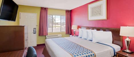 A hotel room with a bed, a desk, a television, and a window with curtains.