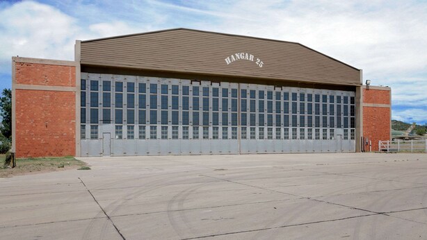 A large, single-story building with a flat roof and a sign reading "HANGAR 25" above the entrance.