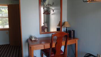 Une pièce comprenant un bureau en bois, une chaise, un miroir, une lampe et un porte-manteau.
