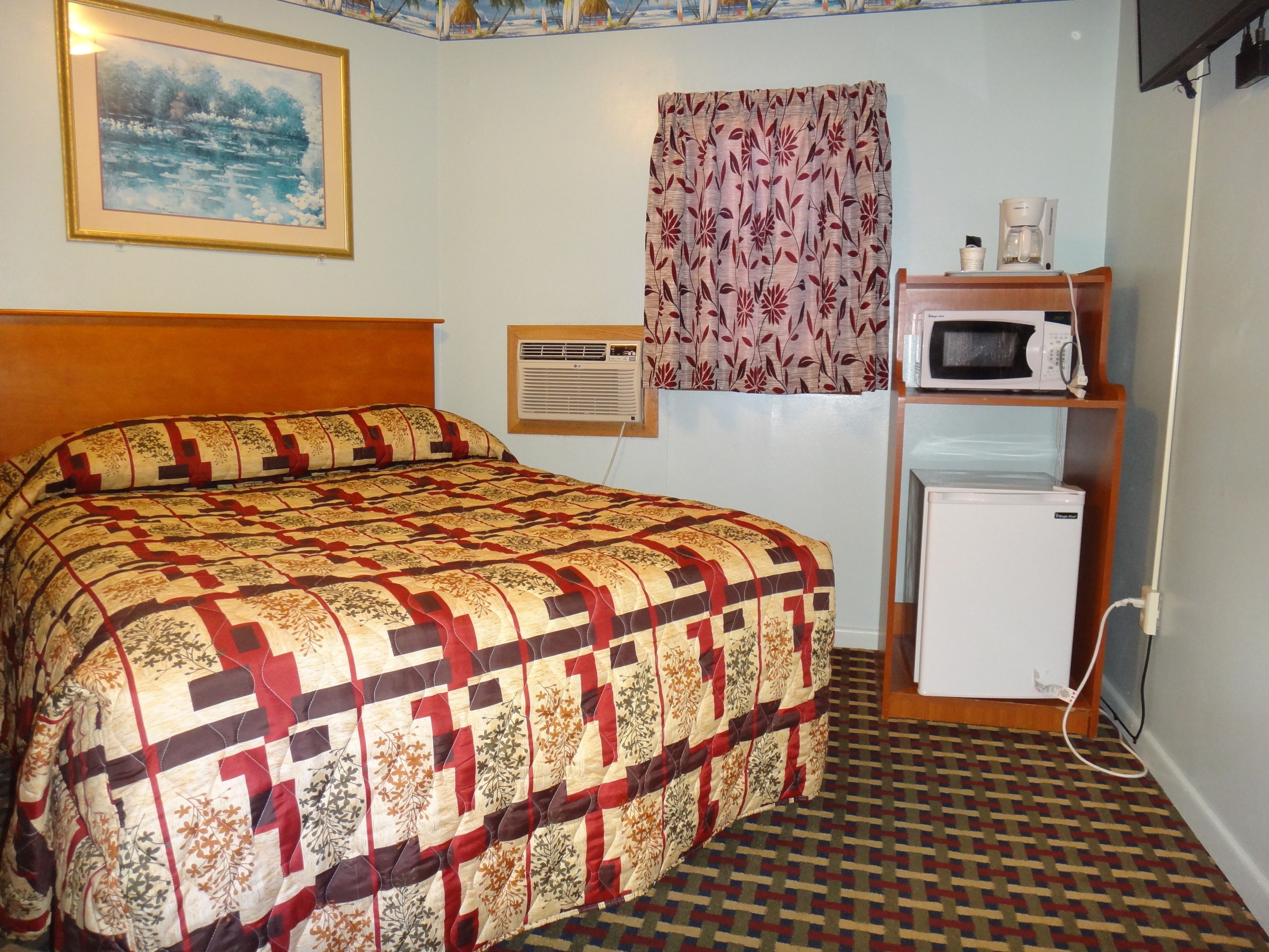 Ein Hotelzimmer mit einem Bett, einem kleinen Kühlschrank, einer Mikrowelle und einem Fenster mit floralem Vorhang.