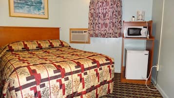 Ein Hotelzimmer mit einem Bett, einem kleinen Kühlschrank, einer Mikrowelle und einem Fenster mit floralem Vorhang.