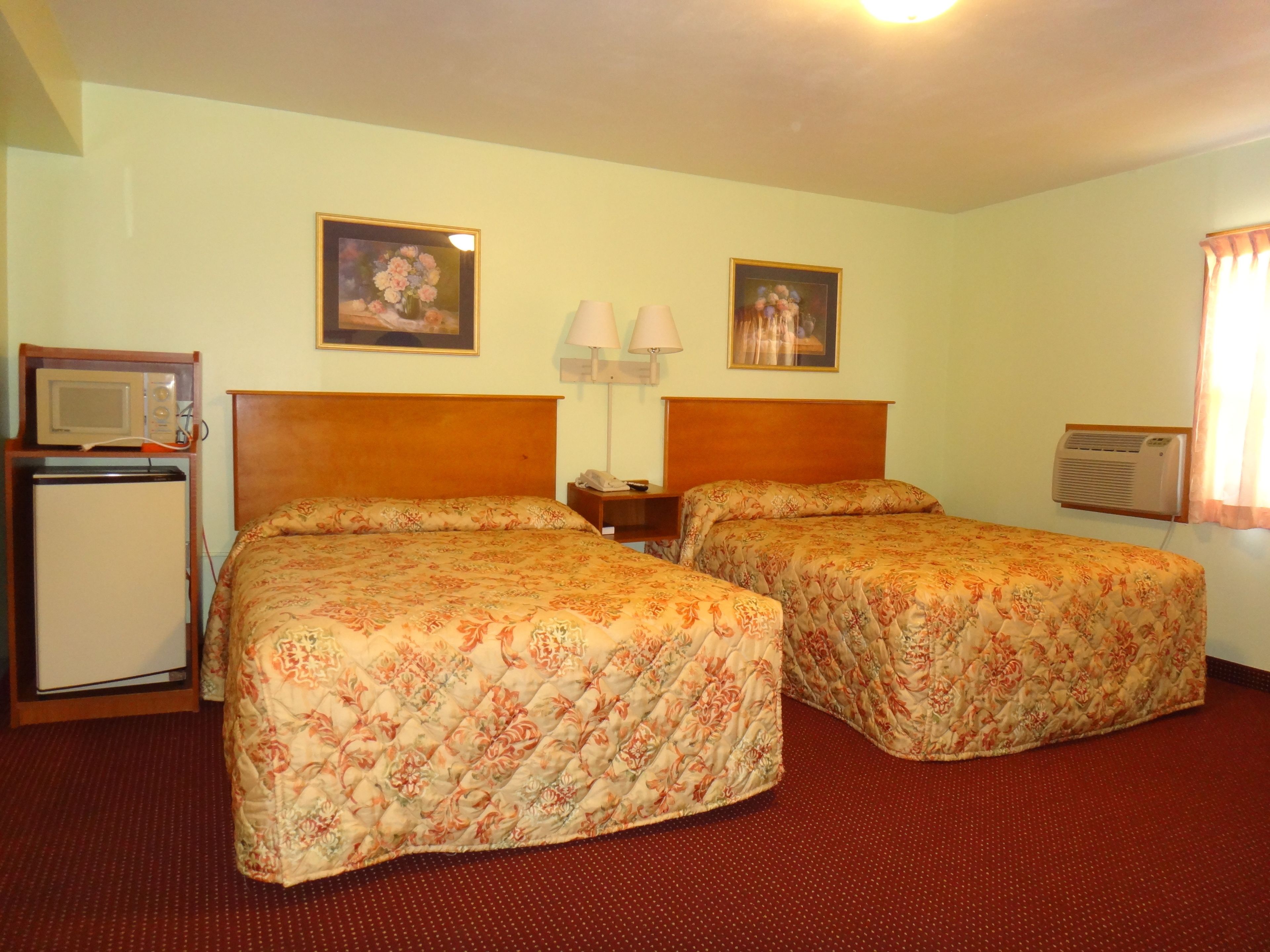 A hotel room with two beds, a small refrigerator, a microwave, a lamp, and an air conditioner.