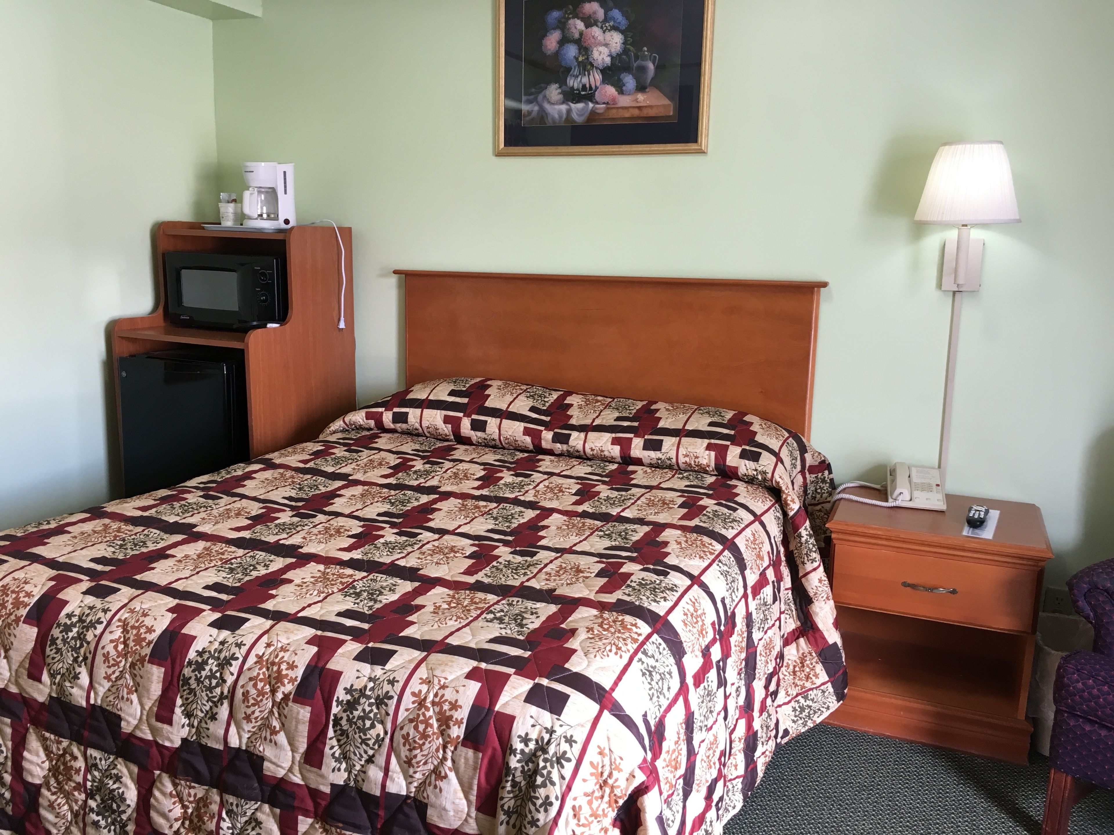 A hotel room with a bed, a nightstand, a lamp, a telephone, a microwave, and a small refrigerator.