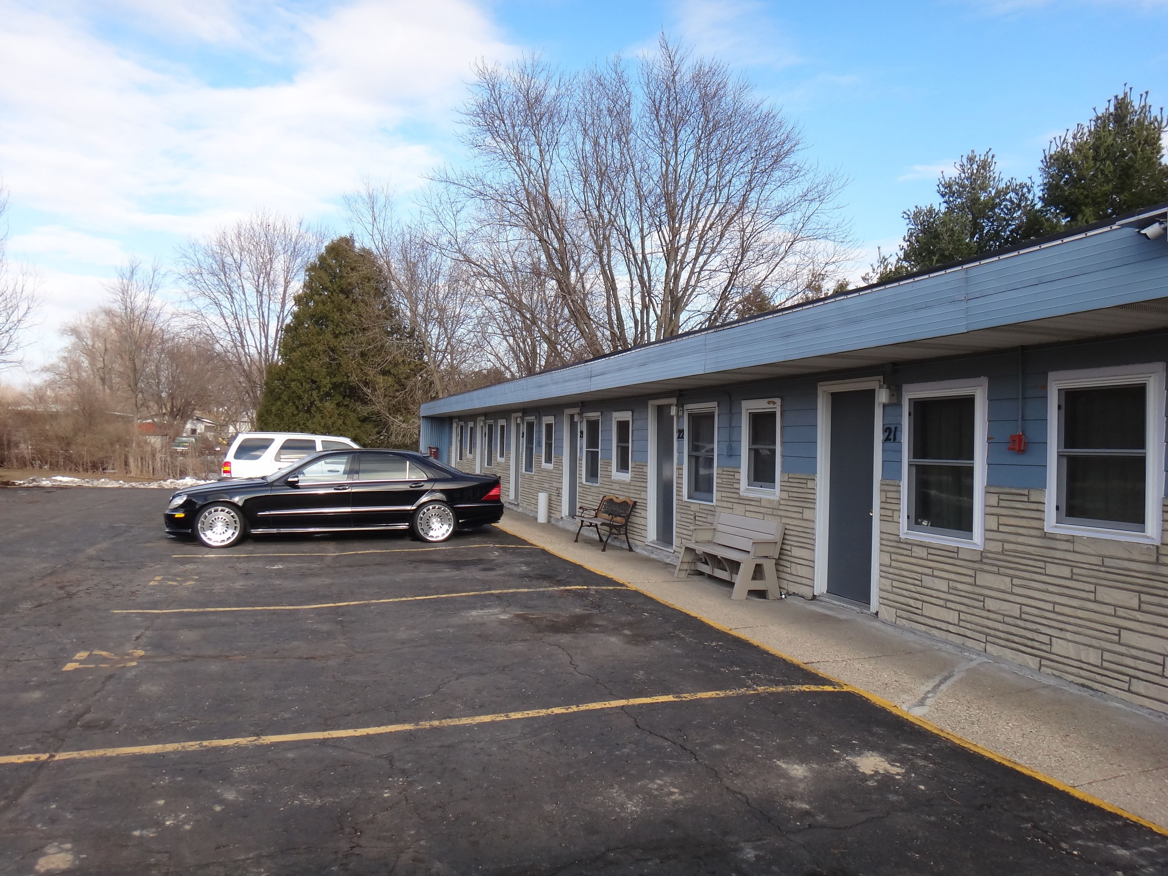 A motel with a row of rooms, a parking lot, and a black car parked in front.