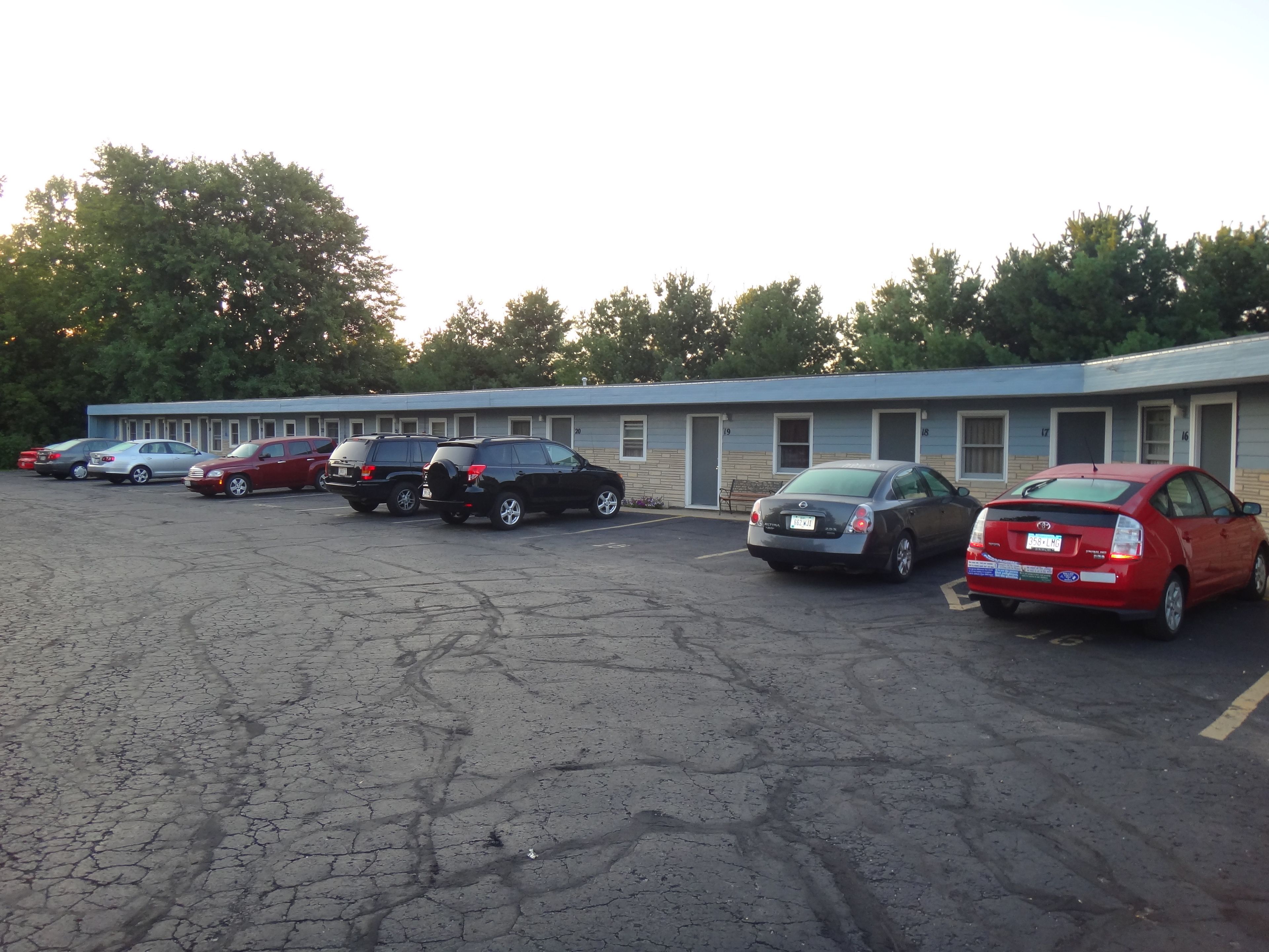 Un parking où plusieurs voitures sont garées devant un motel dont les chambres sont numérotées.