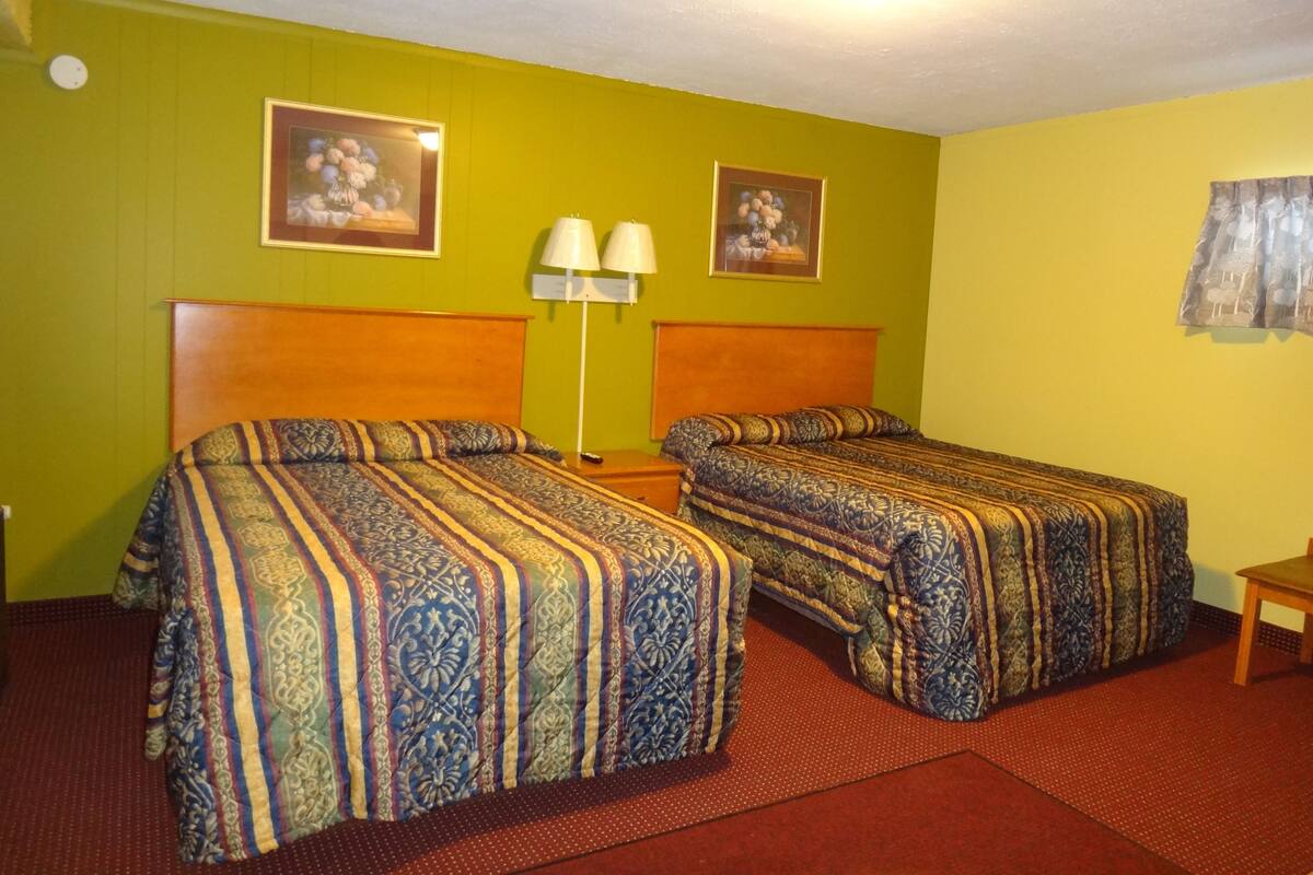 A hotel room with two beds, a nightstand, a lamp, and two framed pictures on the wall.