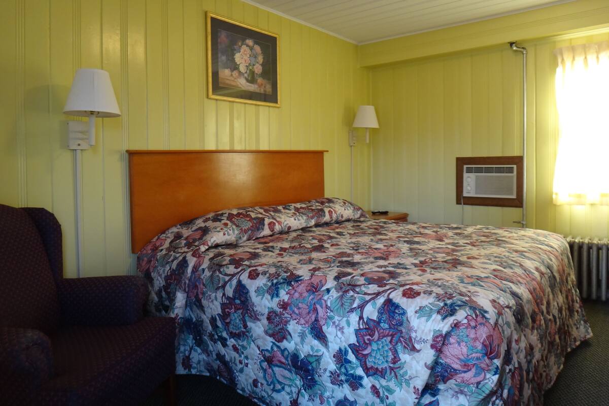 A hotel room with a floral bedspread, a wooden headboard, two bedside lamps, and a framed picture on the wall.