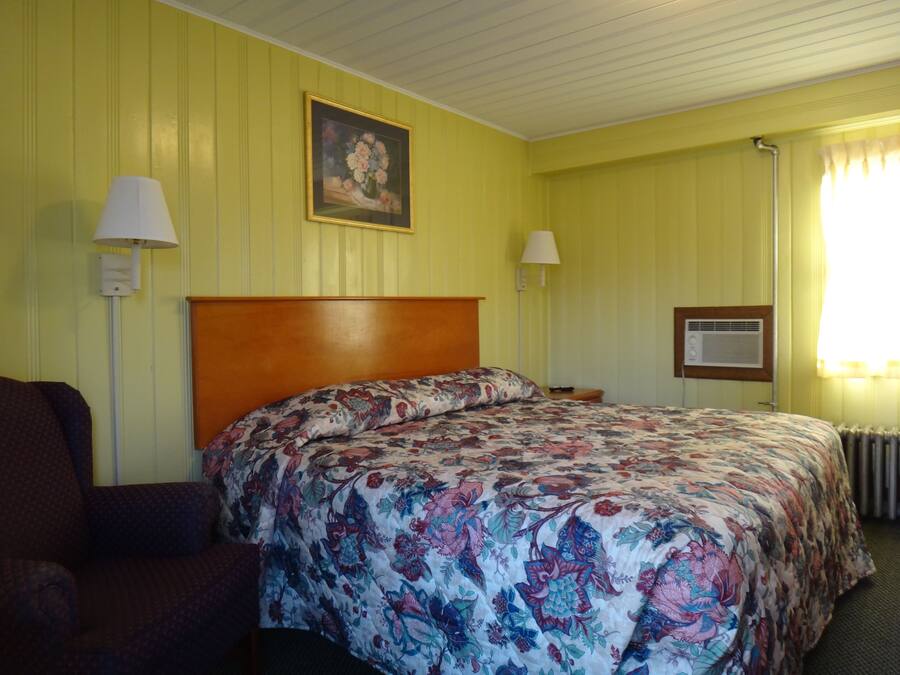A hotel room with a floral bedspread, a wooden headboard, two bedside lamps, and a framed picture on the wall.
