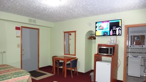 Une chambre d’hôtel comprenant un lit, un bureau avec une chaise, une télévision, un four à micro-ondes et une petite kitchenette.