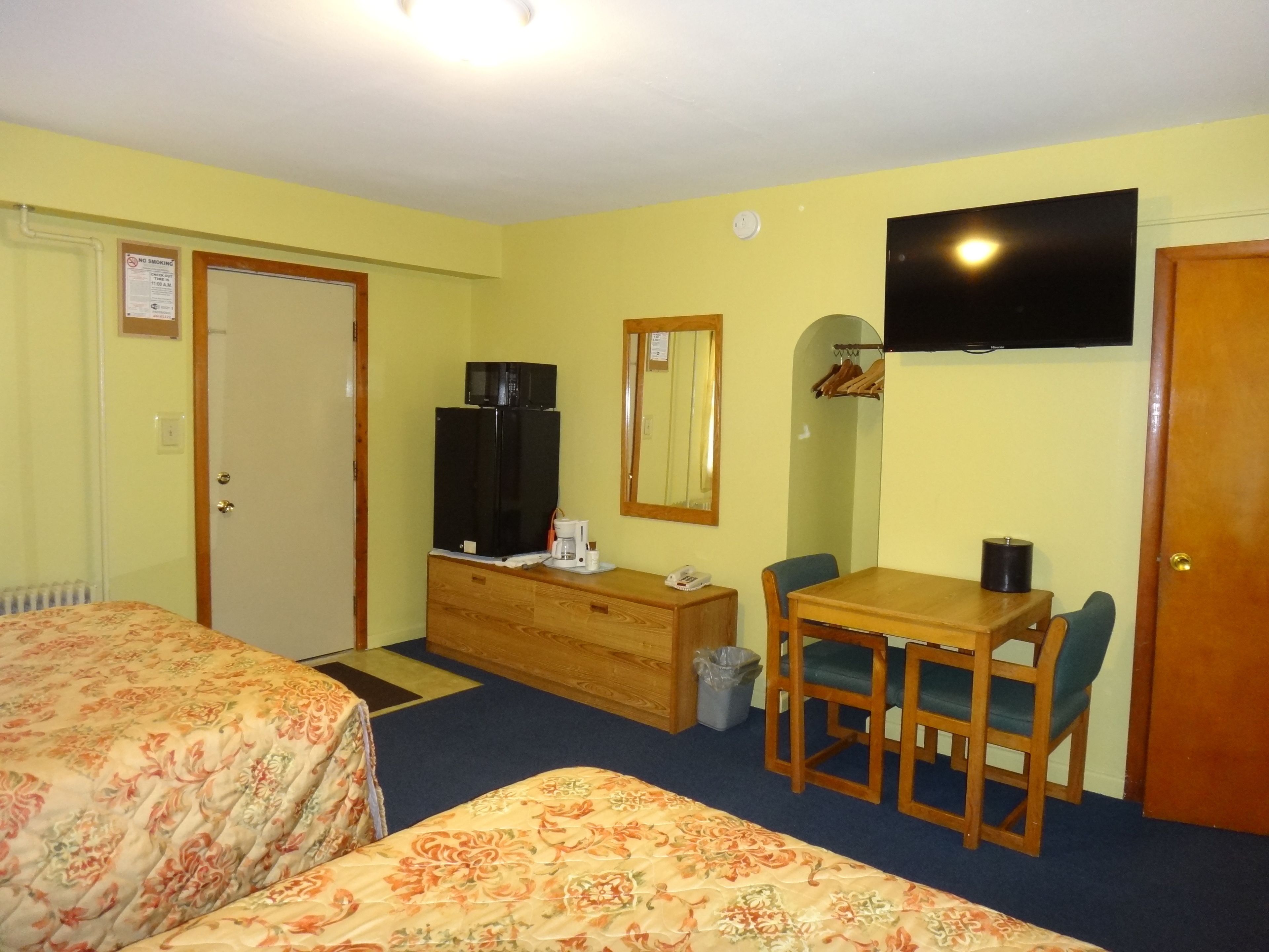 A hotel room with two beds, a wooden dresser, a desk with a chair, a television, and a mirror.