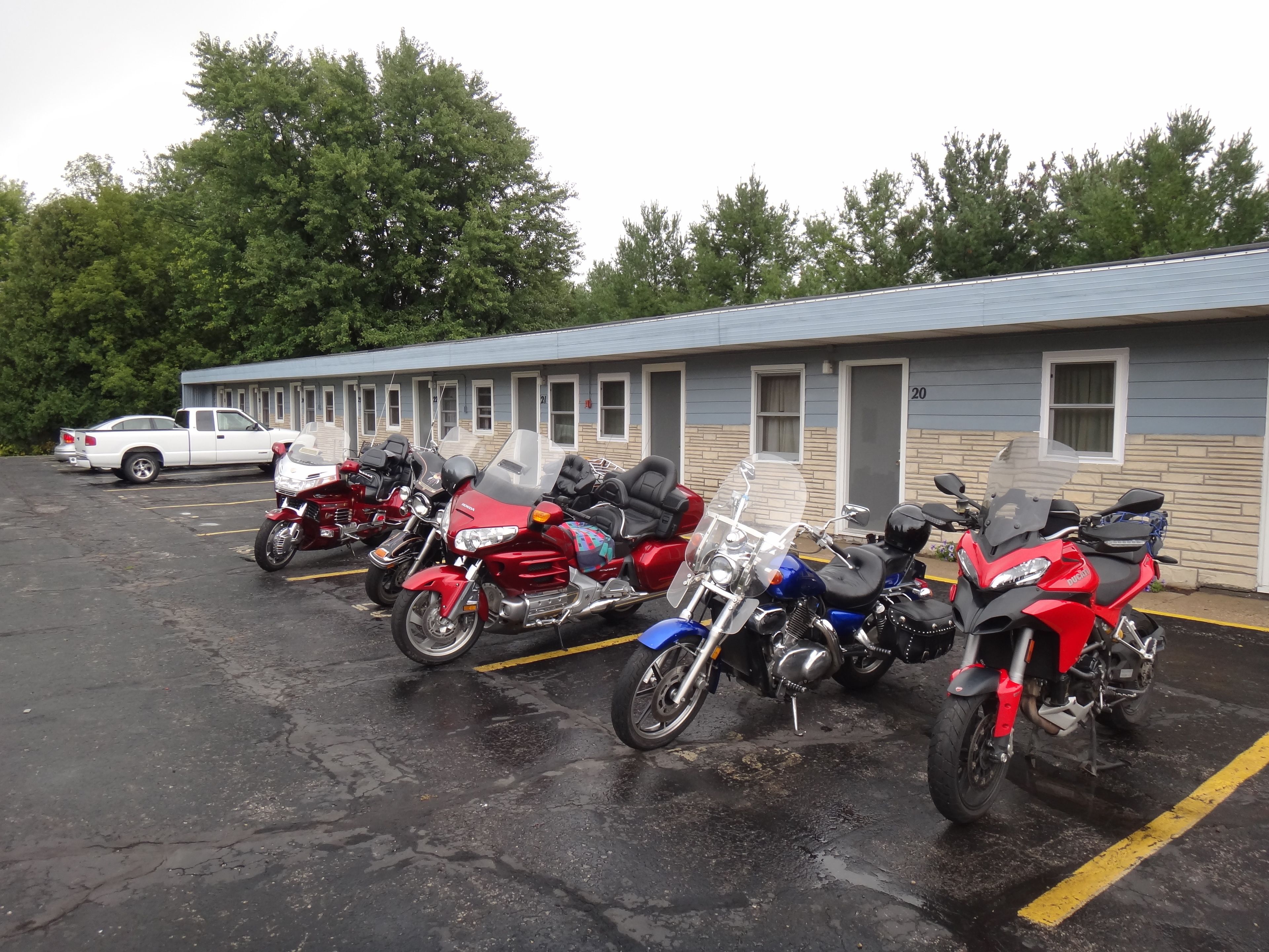 Una fila de motocicletas estacionadas en un estacionamiento frente a un motel de fachada azul y beige.