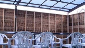 Un espacio de estar techado al aire libre con sillas de plástico blanco y pared de madera.