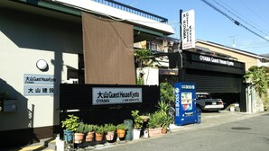 Un edificio con el letrero de Guest House Kyoto Oyama, una máquina expendedora azul y plantas en macetas al frente.