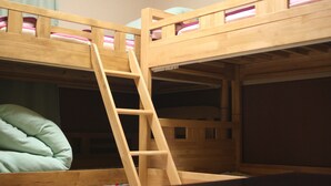 Una cama litera con escalera de madera, almohada verde y ventana con cortinas.