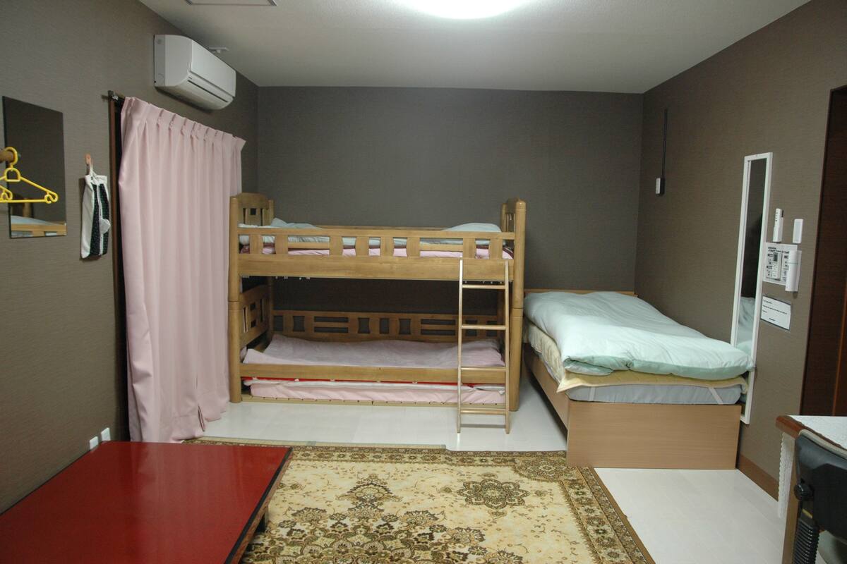 Una habitación pequeña y funcional con dos literas, un escritorio de madera, un espejo y un armario pequeño.
