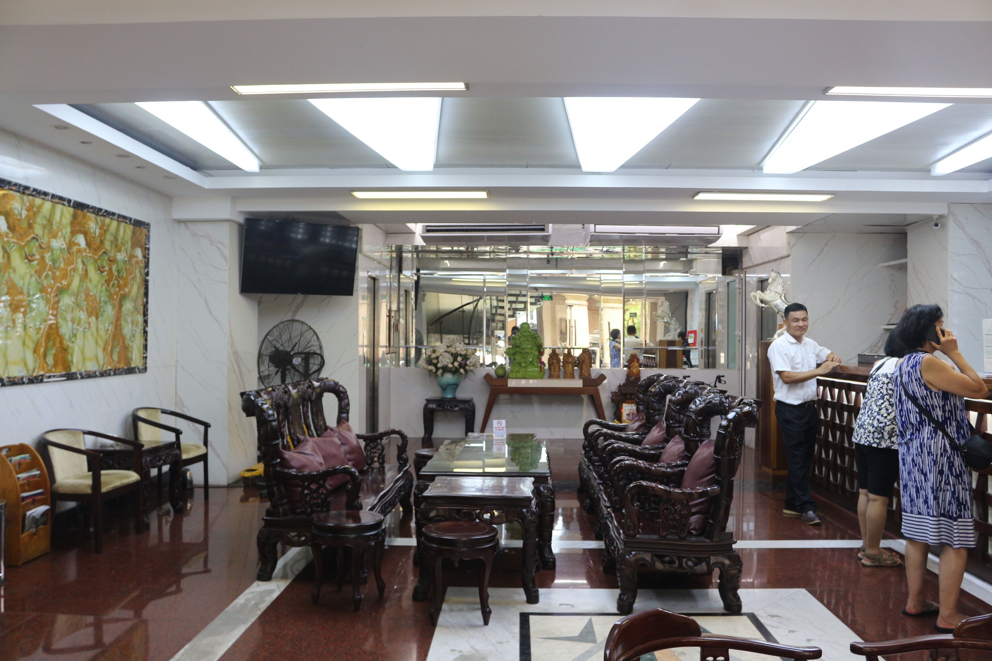 A lobby with a marble floor, wooden furniture, a large painting, a television, and a glass partition.