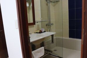 Bathroom features a glass shower enclosure, a white sink with a mirror, and a tiled wall with a two-tone pattern.
