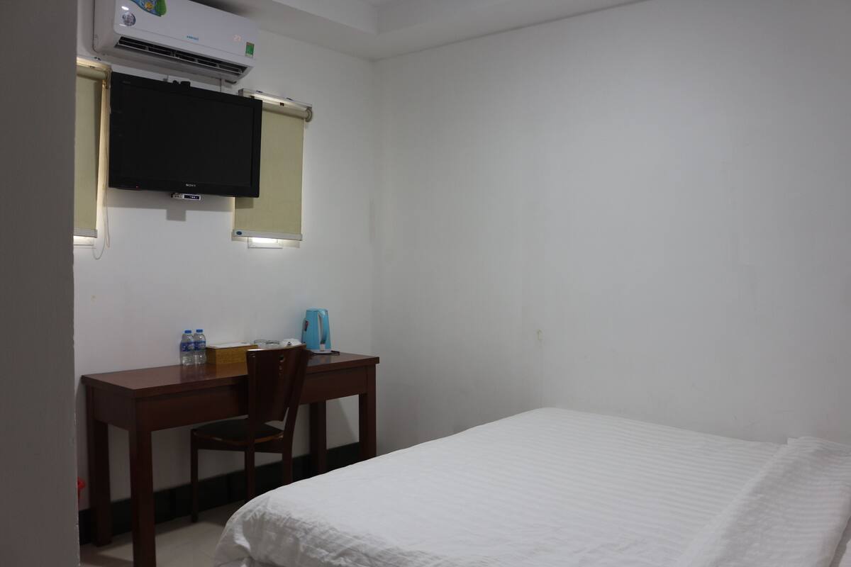 Une chambre d’hôtel équipée d’un lit, d’un bureau avec une chaise, d’une télévision et d’un appareil de climatisation.