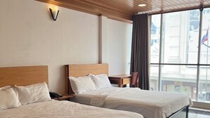 Hotellihuone, jossa on kaksi sänkyä, puinen katto, suuret ikkunat ja näkymä kaupunkiin.
