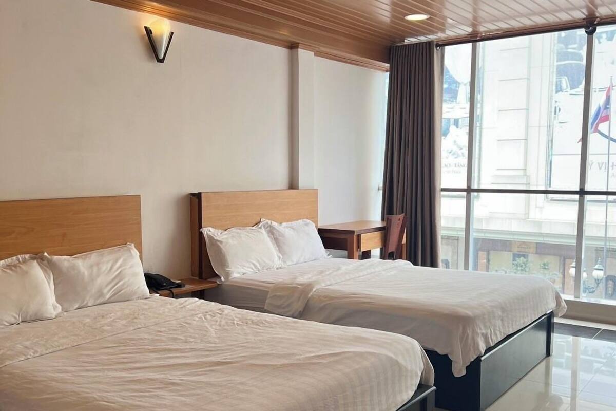 Une chambre d’hôtel avec deux lits, un plafond en bois, de grandes fenêtres et une vue sur la ville.