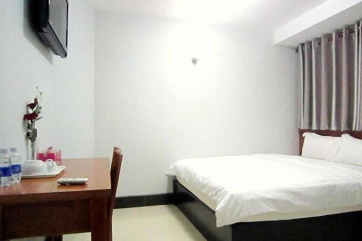 Une chambre d’hôtel avec un lit, un bureau et une chaise, une petite table avec un vase de fleurs et un téléviseur fixé au mur.