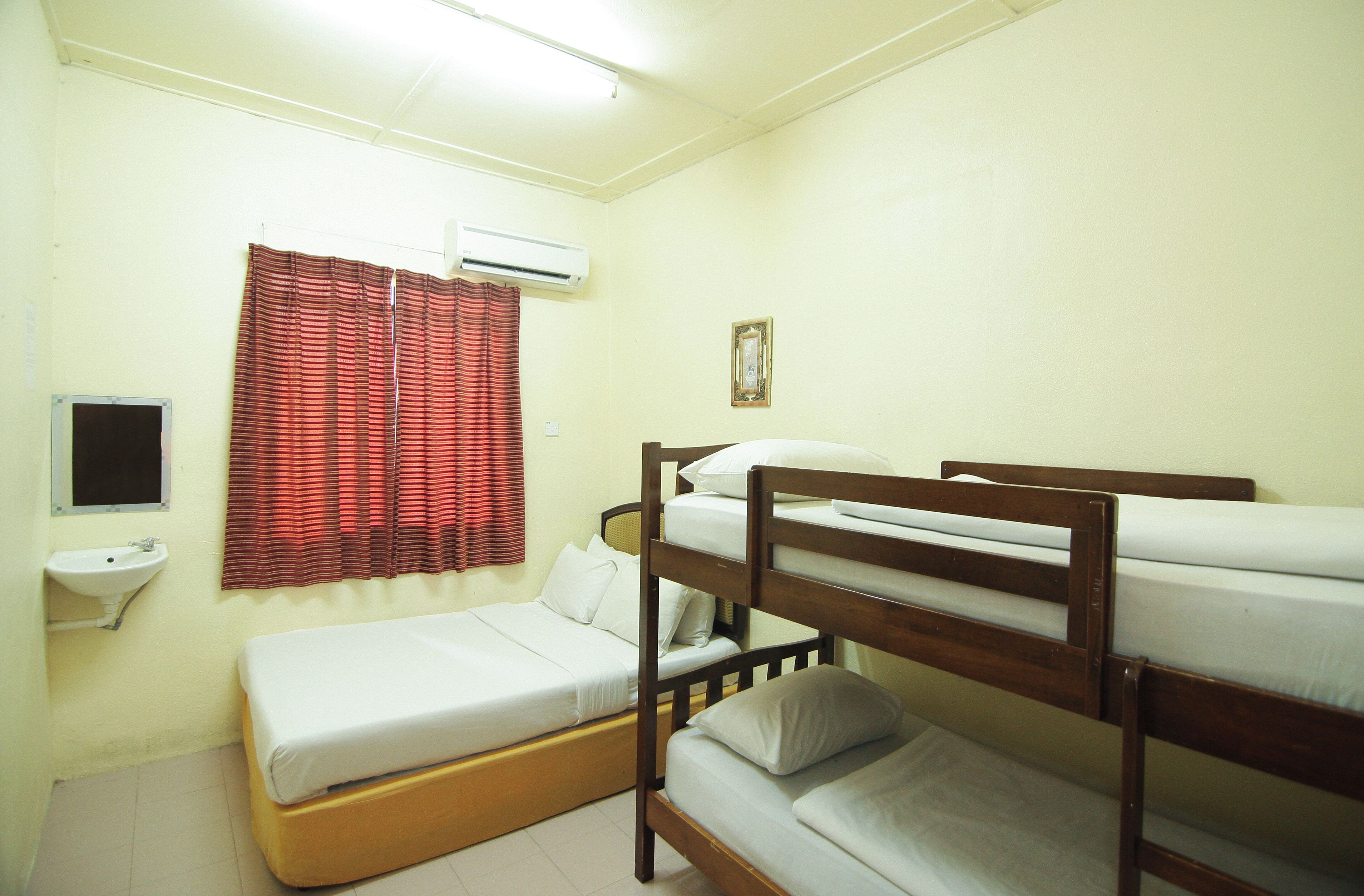 Une chambre de dortoir avec des lits superposés, un lit simple, une fenêtre avec des rideaux rouges, un climatiseur, un lavabo et un tableau encadré au mur.