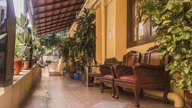 A corridor with tiled flooring, wooden chairs, and potted plants. - Anggerik Lodging Hotel (George Town)
