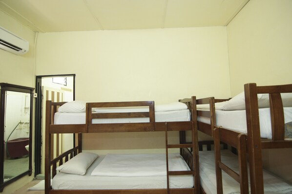 A bunk bed room with a wooden frame, white bedding, and a visible bathroom with a red tub.