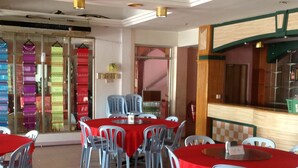 A dining area with round tables covered in red tablecloths and surrounded by plastic chairs. - Hosaga Biz Hotel (KELANTAN)
