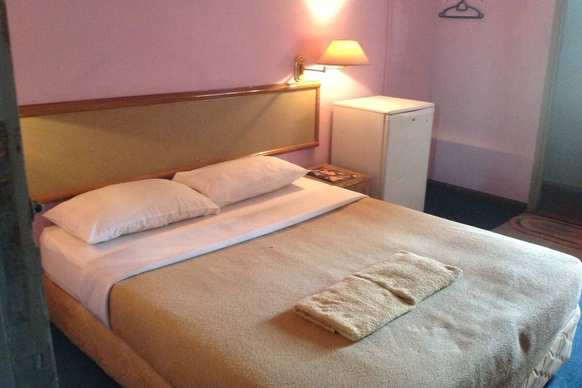 Een hotelkamer met een bed, nachtkastje, lamp, kledingkast en hanglamp.