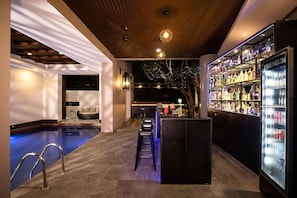 Un área de bar con piscina, taburetes y un refrigerador lleno de bebidas.
