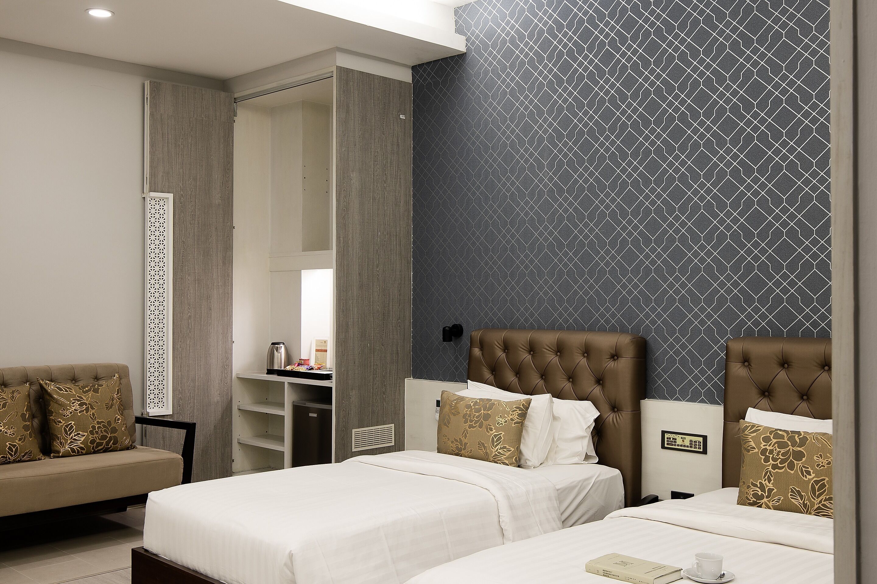 A hotel room with a bed, a desk, and a chair. There is a wardrobe and a mirror.